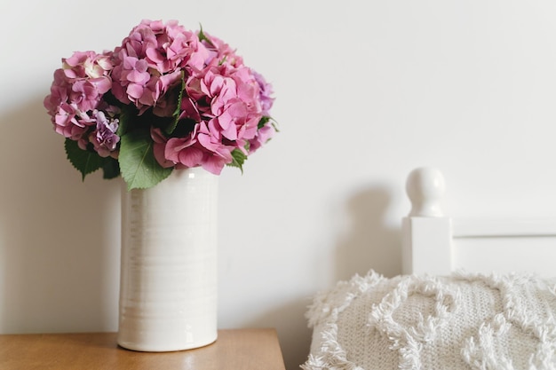 Ramo de hortensias en jarrón almohada blanca en la cama sobre fondo de pared blanca con espacio de copia Hermosas flores de hortensias rosas y moradas en casa Feliz día de las madres