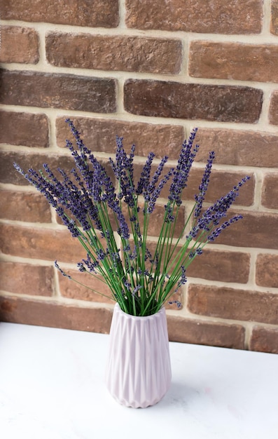 Un ramo de lavanda fresca en un jarrón junto a la ventana Flores en el fondo de una pared de ladrillos