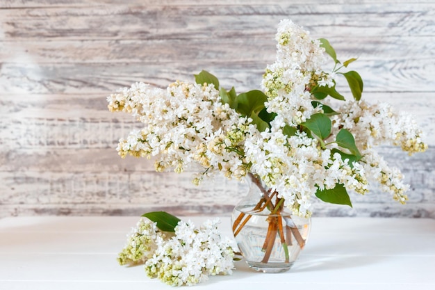 Ramo lila blanco en jarrón de vidrio sobre mesa de madera Ramas primaverales de ramo de flores festivo lila floreciente con espacio de copia