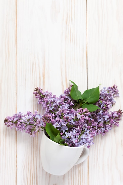 Un ramo de lilas fragantes frescas en una taza blanca de la porcelana en un fondo de madera blanco.