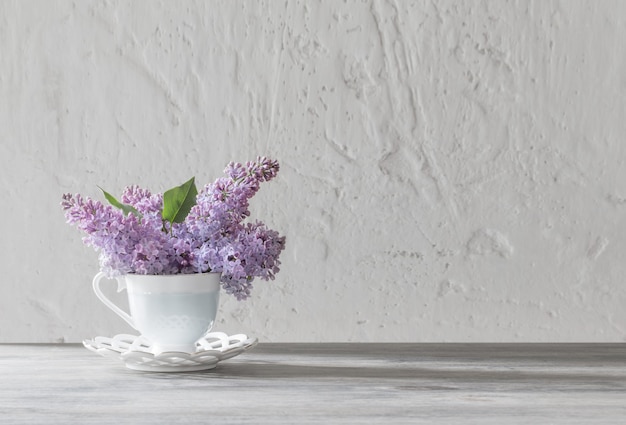 Ramo de lilas en taza de cerámica sobre mesa de madera antigua