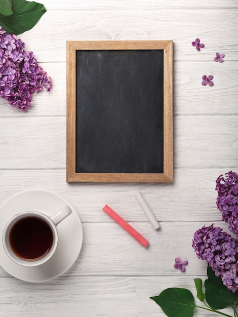 Un ramo de lilas con la taza de té, tablero de tiza en los tableros blancos. Día de la Madre