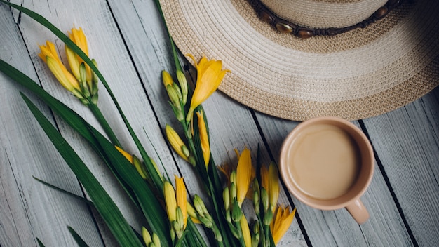 Un ramo de lirios amarillos, un sombrero y una taza de café en una mesa de madera, desayuno