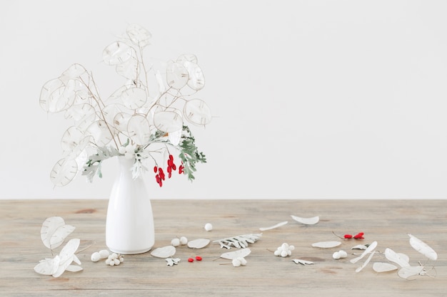 Ramo con lunaria y frutos rojos en jarrón blanco sobre lengüeta de madera