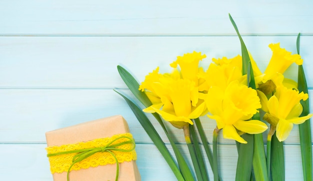 Foto un ramo de narcisos amarillos y una caja de regalo con un regalo sobre una mesa de madera.