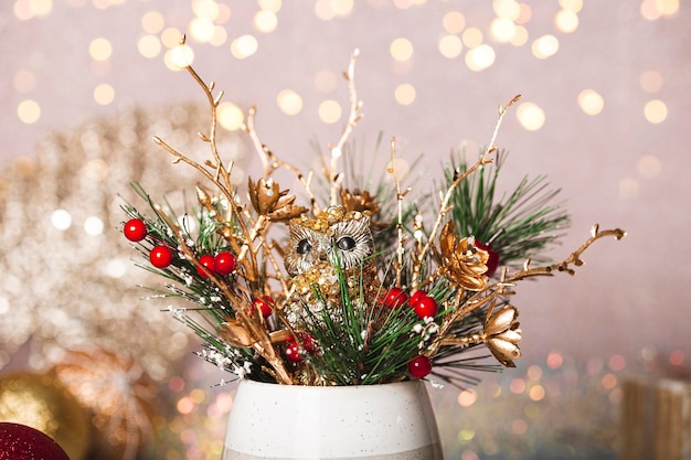 Ramo de Navidad festivo con ramas de abeto decoraciones doradas y un juguete de búho de Año Nuevo en la mesa de cerca