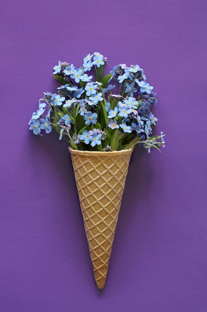 Un ramo de nomeolvides en un cono de galleta sobre un fondo violeta como helado