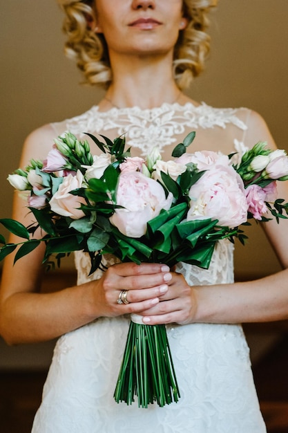 Ramo de novia Boda La chica con un vestido blanco de pie sobre un fondo marrón y sostiene un hermoso ramo de flores rosas blancas y vegetación