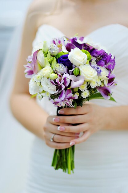 Ramo de novia de flores blancas y lilas en manos de la novia