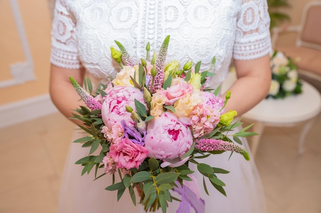 Ramo de novia Hermosas flores de boda rosadas en manos de la novia Estudio interior de primer plano disparó contra un fondo brillante Ramo con peonías eustoma y eremurus