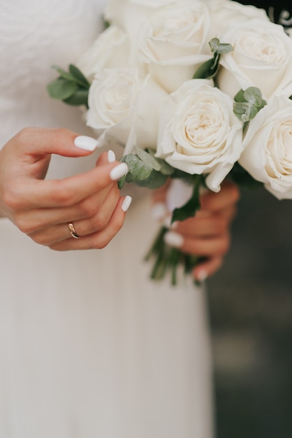 Ramo de novia y la mano de la novia con manicura blanca de cerca