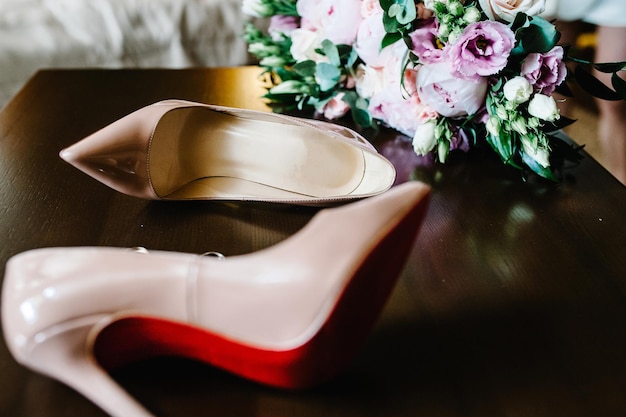 Ramo de novia de la novia de flores rosadas rosas y verdes elegantes zapatos beige lacados clásicos elegantes y anillos de oro sobre fondo de madera Cerrar