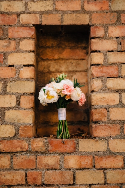 Ramo de novia de peonías blancas y rosas eryngium y capullos verdes con cintas blancas sobre un ladrillo