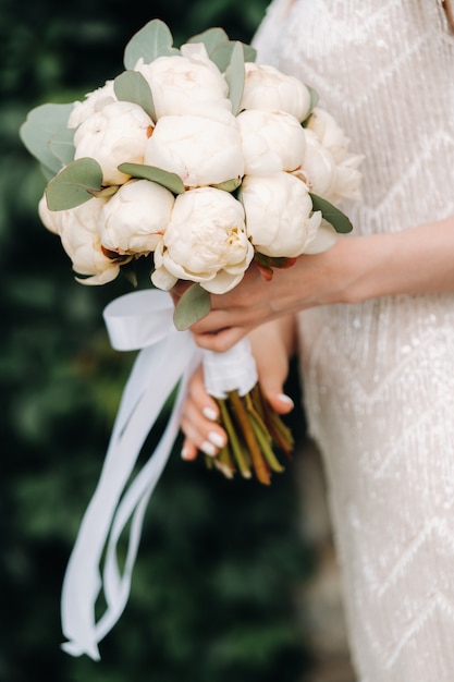 Ramo de novia con peonías en manos de la novia en la boda.