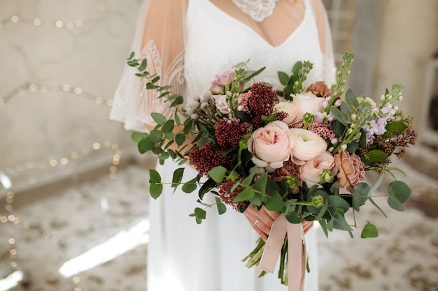 Ramo de novia con peonías rosas y rosas en las manos de la novia