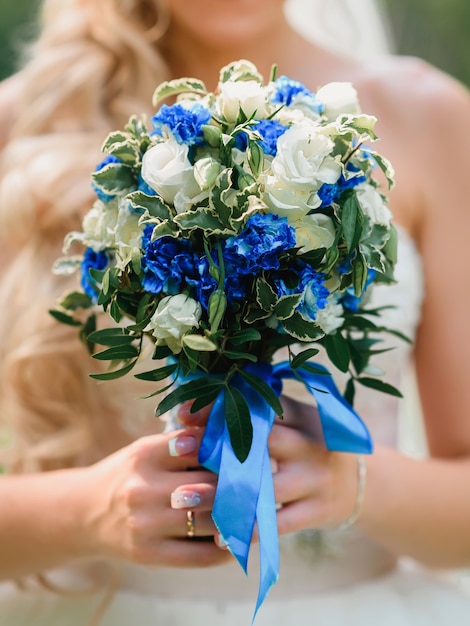 Ramo de novia con rosas blancas y flores azules en las manos