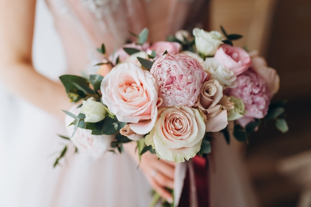 Ramo de novias con peonías, fresias y otras flores en manos de las mujeres. Color primaveral claro y lila. Mañana en la habitación