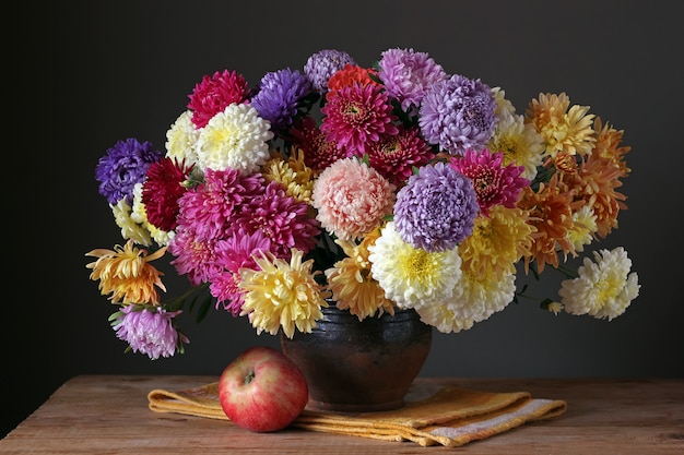 Ramo otoñal de asters y crisantemos. Bodegón con flores y manzana.