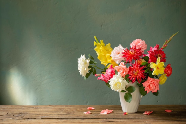 Ramo de otoño con flores rojas y amarillas en jarrón blanco sobre fondo oscuro