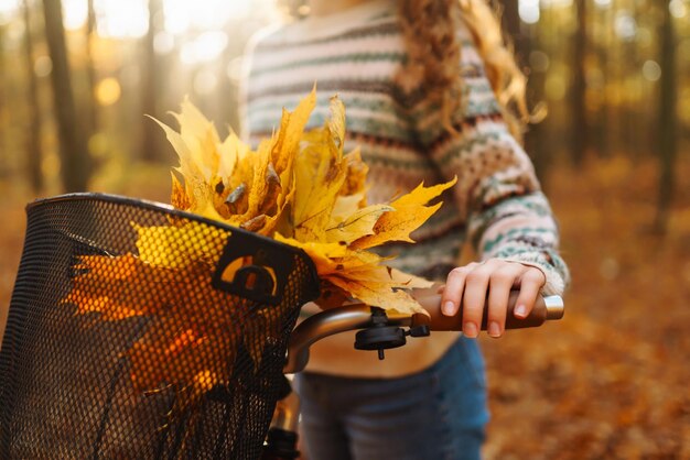 Foto ramo de otoño de hojas amarillas y naranjas en una canasta de bicicleta en un parque de otoño soleado