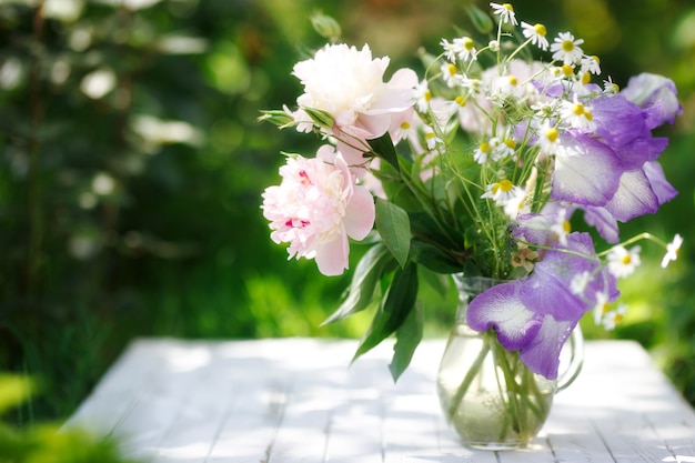 Ramo de peonías blancas, manzanillas y flores de iris en jarrón de cristal. Fondo de verano.