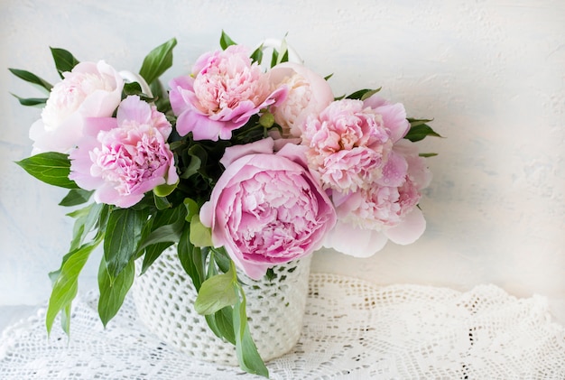 Ramo de peonías rosas sobre una mesa de madera en una cesta hecha a mano sobre mantel de encaje