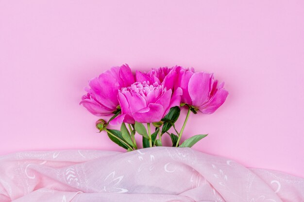 Ramo de primer plano de flores de peonía rosa oscuro y tela rosa sobre fondo rosa con espacio de copia