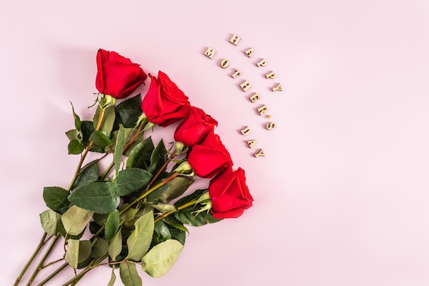 Un ramo rojo de rosas escarlatas frescas sobre un fondo rosa con el texto de letras de madera de feliz día de la madre vista superior postal de estilo plano