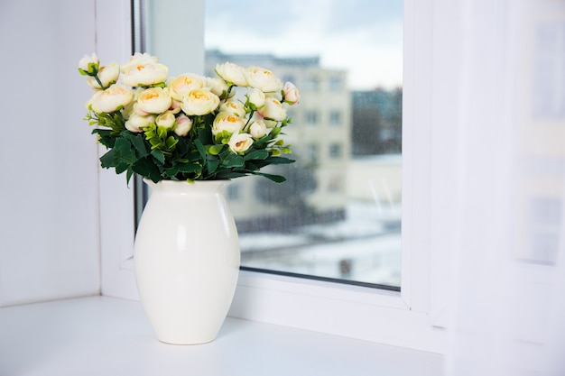 Ramo de rosas amarillas en jarrón de cerámica en una ventana