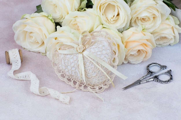 un ramo de rosas blancas, un corazón de encaje, tijeras y una cinta de encaje