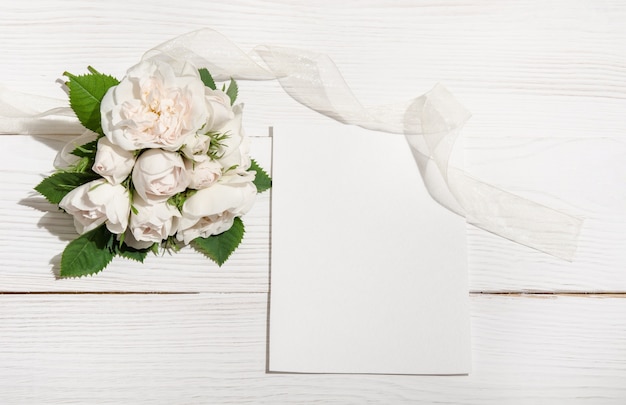 Ramo de rosas blancas sobre mesa blanca con tarjeta vacía. vista superior