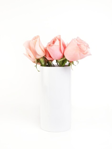 Ramo de rosas en un florero de cerámica blanca sobre un fondo blanco.