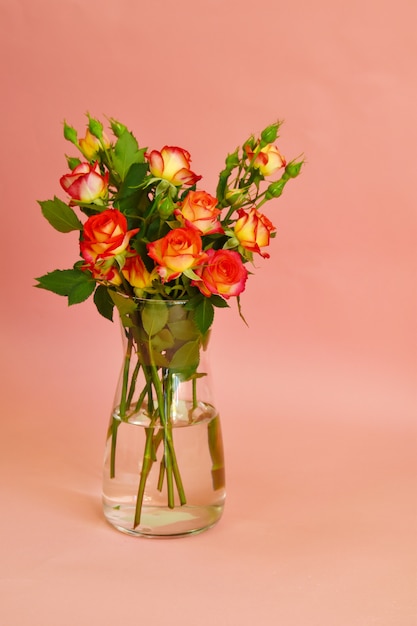 Un ramo de rosas en florero de vidrio sobre fondo rosa.