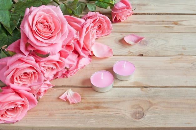 Ramo de rosas frescas y velas sobre fondo de madera