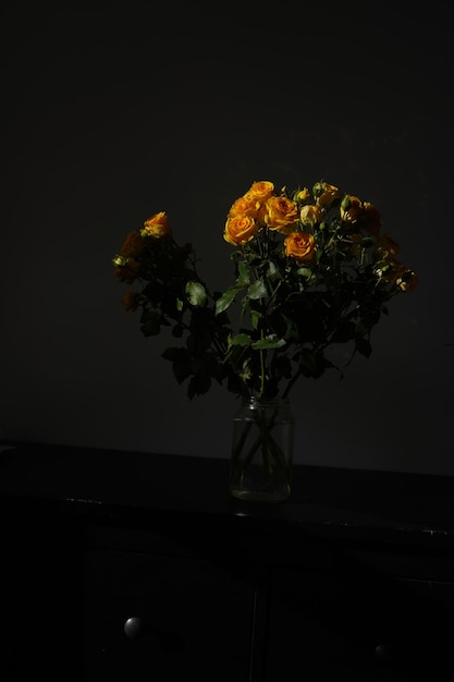 Foto un ramo de rosas naranjas a la luz del sol sobre un fondo negro.