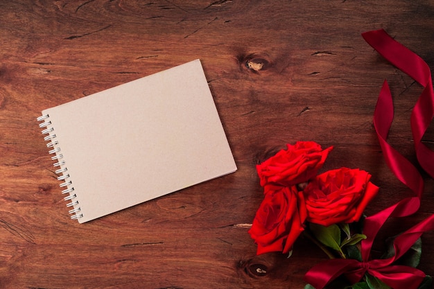 Ramo de rosas rojas y un bloc de notas en blanco sobre un fondo de madera con textura