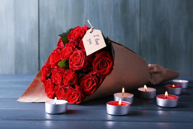 Ramo de rosas rojas con etiqueta envuelta en papel y velas sobre fondo de madera