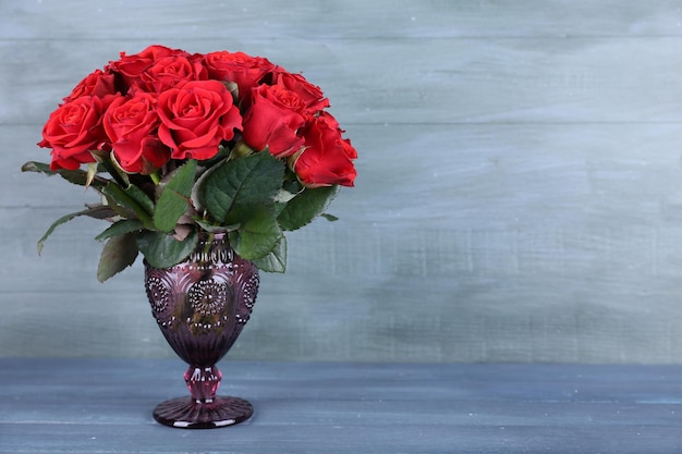 Ramo de rosas rojas en jarrón de cristal sobre fondo de madera