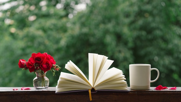 Foto un ramo de rosas rojas en un jarrón y un libro en un alféizar de madera