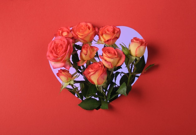 Ramo de rosas rojas en un marco de papel en forma de corazón sobre una superficie roja