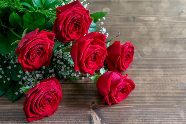 Ramo de rosas rojas en la mesa de madera en sunlights en ángulo. Bonito regalo para saludar con San Valentín.