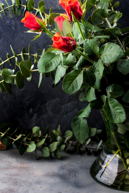 Ramo de rosas rojas y muchas hojas verdes en un jarrón sobre un fondo negro