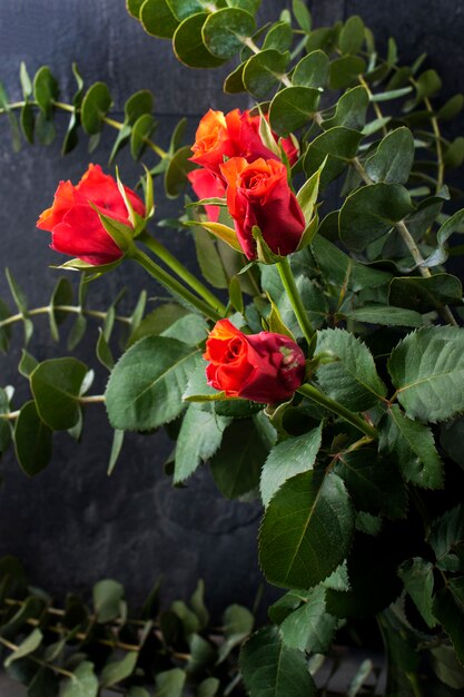 Ramo de rosas rojas y muchas hojas verdes en un jarrón sobre un fondo negro