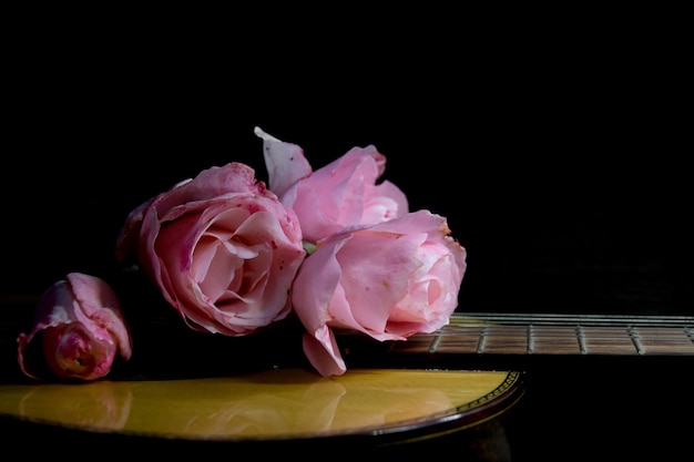 Foto un ramo de rosas rosadas en las cuerdas de la guitarra sobre un fondo negro