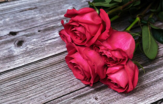 Ramo de rosas rosadas rojas sobre una superficie de madera con un lugar para el texto