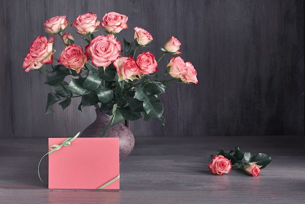 Ramo de rosas rosadas sobre fondo rústico oscuro con espacio de copia en tarjeta de papel en blanco