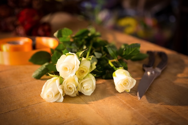 Ramo de rosas con tijeras y cinta de polietileno en la mesa de madera