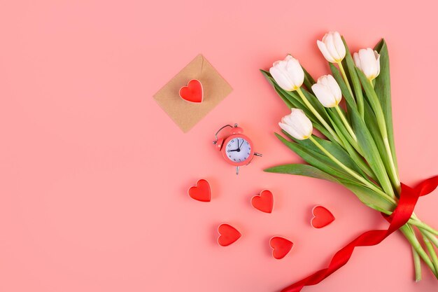 Ramo de sobres de corazones de tulipanes blancos y un reloj sobre un fondo rosa pastel aislado