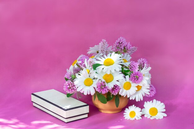 Foto ramo de trébol y manzanilla en un jarrón sobre un fondo claro. ramo de verano de flores de jardín y campo. naturaleza muerta sobre fondo rosa.