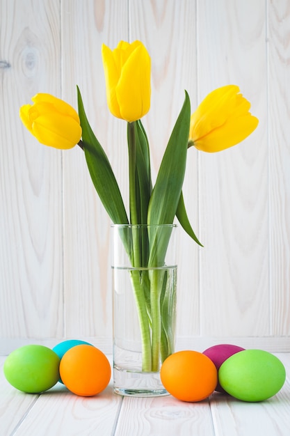 Ramo de tulipanes amarillos y coloridos huevos de Pascua en un fondo de madera clara. Tarjeta de felicitación pascual con flores de primavera.